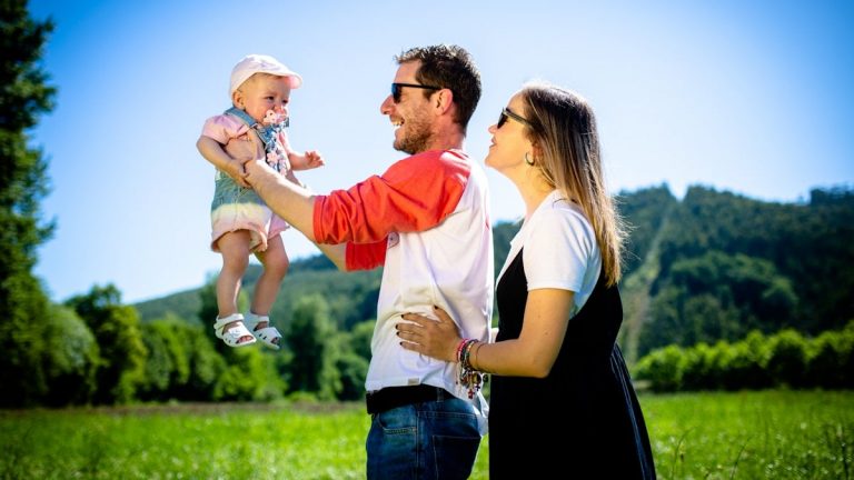 man in white and red polo shirt carrying girl in blue denim jeans during daytime